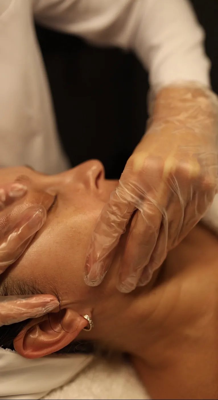 Both gloved hands supporting the cheek and jawline during the external portion of a buccal massage